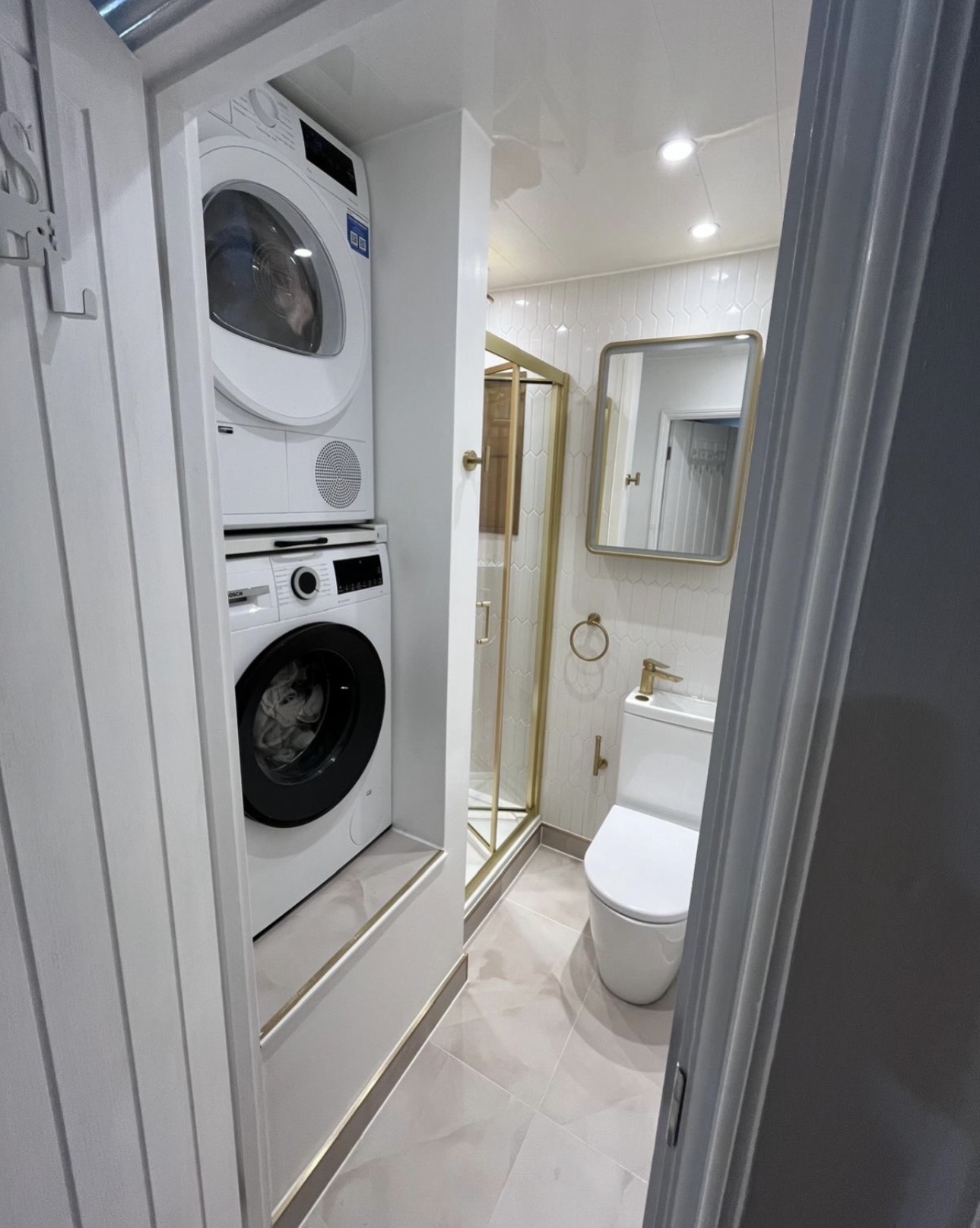 Upstairs bathroom and integrated utility area with stacked washer dryer and brass shower screen in Birmingham by M3 Trades