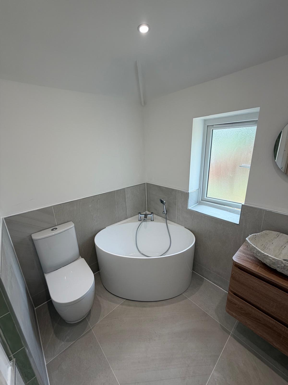 Corner bath with grey stone-effect tiles, walnut vanity and stone vessel basin in a recently completed Rubery Birmingham bathroom by M3 Trades