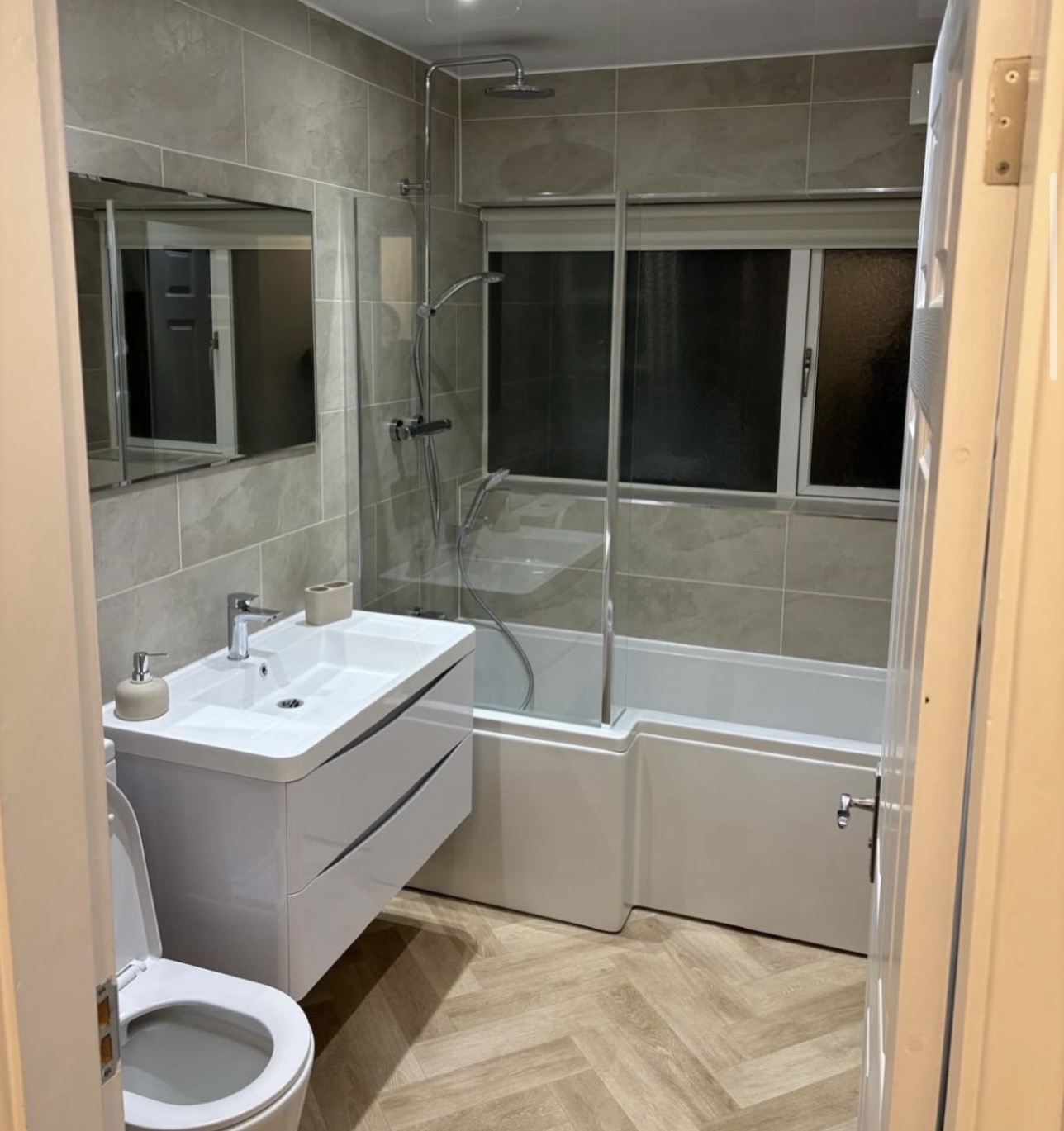 Family bathroom with L-shaped shower bath, stone-effect tiles and herringbone flooring in Birmingham by M3 Trades