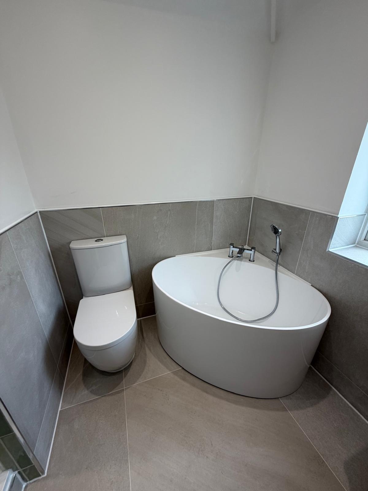 Space-saving corner bath and rimless WC on large grey porcelain tiles installed in Rubery Birmingham by M3 Trades
